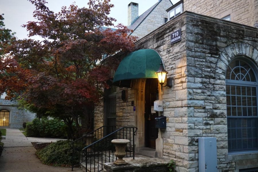 A photograph of a stone building with a green awning on its entrance and a black sign reading “710 Emerson.” A red tree is in the background.