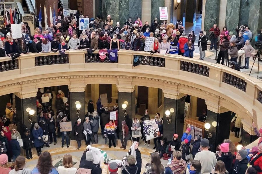 Protestors gather in a domed multi-story building holding signs advocating for abortion access.