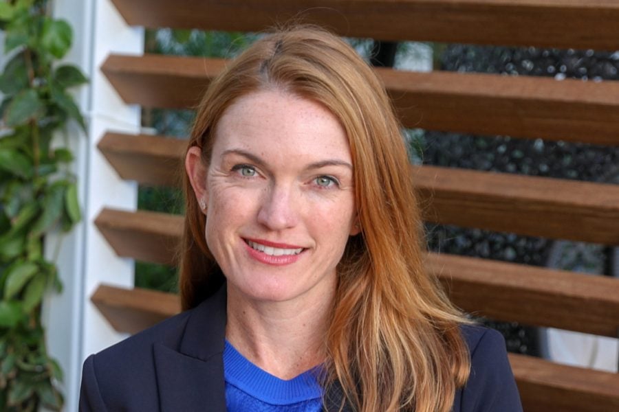 A white lady with green eyes and red hair wearing a dark suit jacket over a blue shirt.