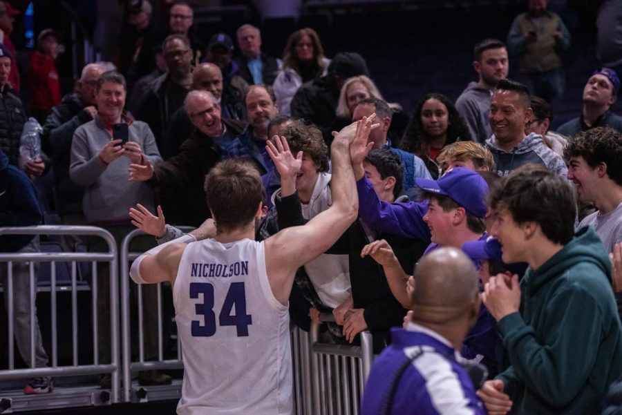 A basketball player in a purple and white jersey high-fives fans in the stands.