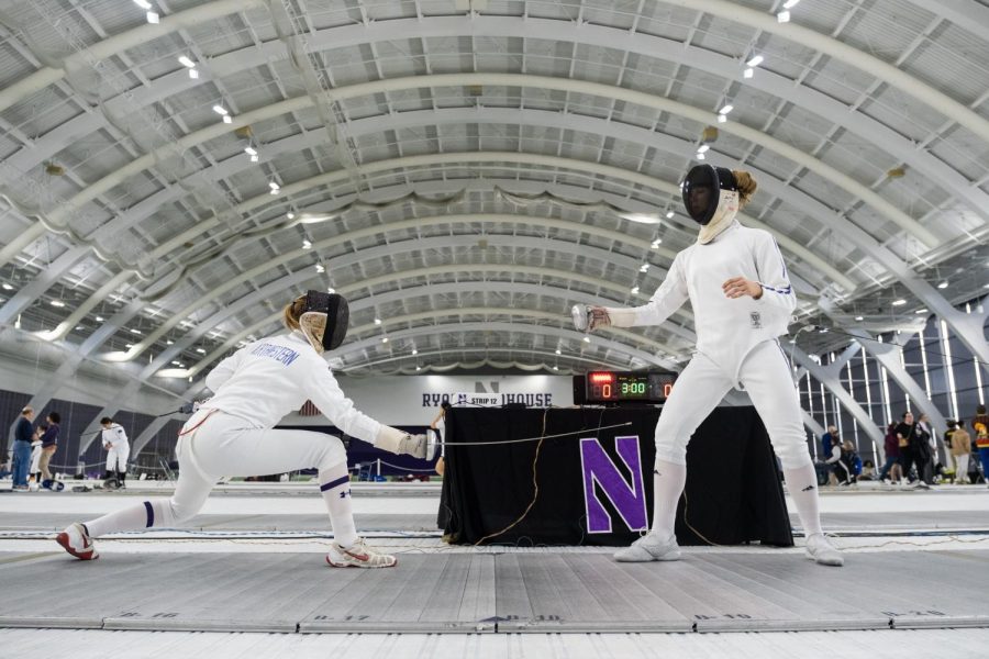 Two athletes, in white fencing suits, face each other on a mat.