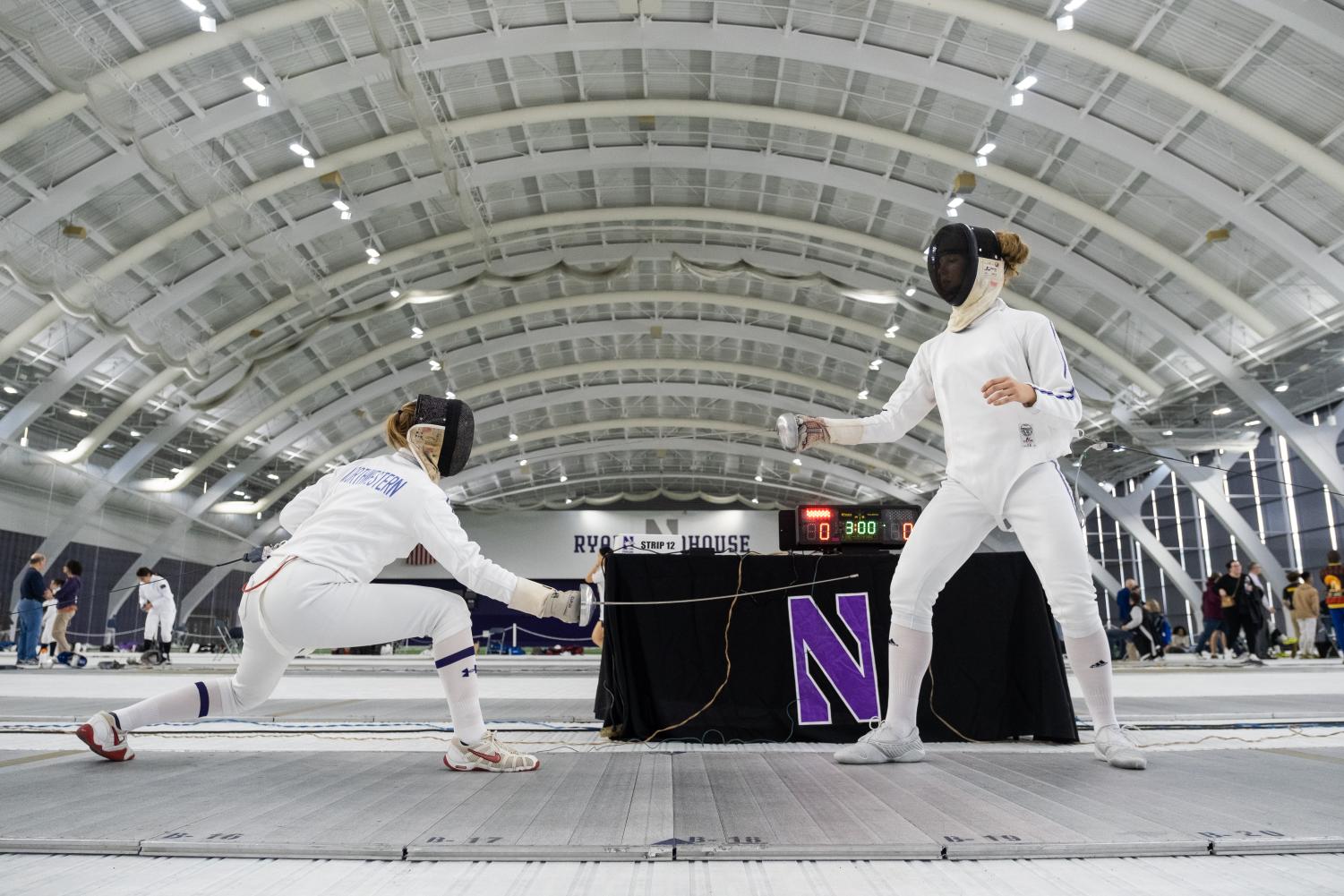 Two+athletes%2C+in+white+fencing+suits%2C+face+each+other+on+a+mat.