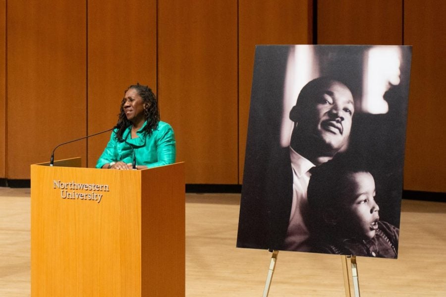 A woman in a green top stands at a podium next to a photo of a man and child.
