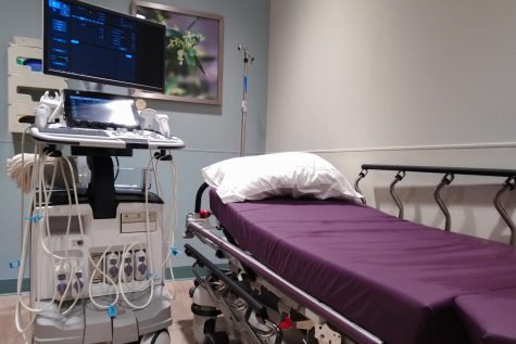 A computer with ultrasound probes is on the left, a purple bed on the right.