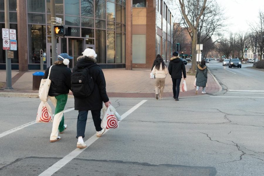 Two pairs of pedestrians are crossing the road and carrying white plastic bags from Target.