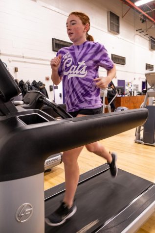 Girl runs on treadmill in purple “the Cats” shirt.