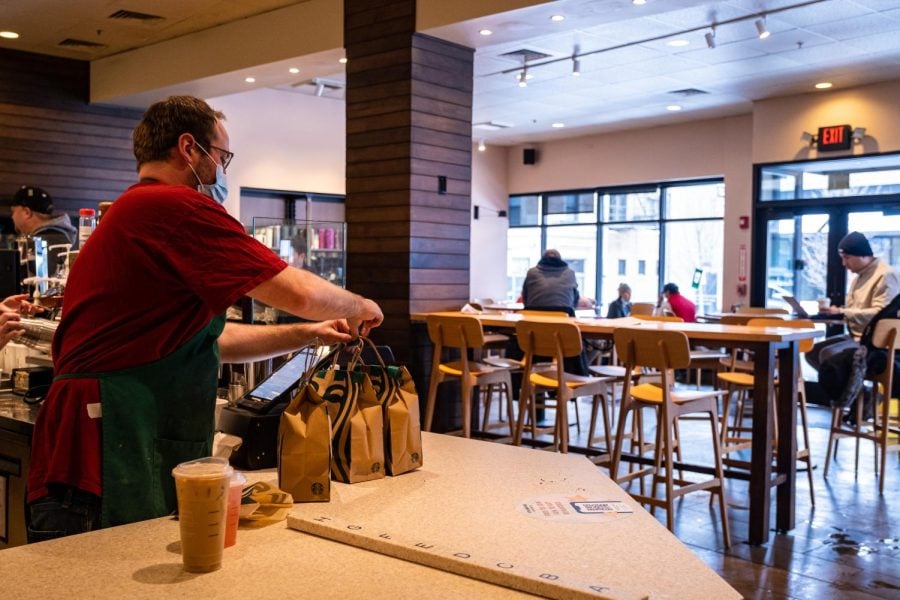 A Starbucks employee in a red shirt places bags with the Starbucks logo on a counter in the store.