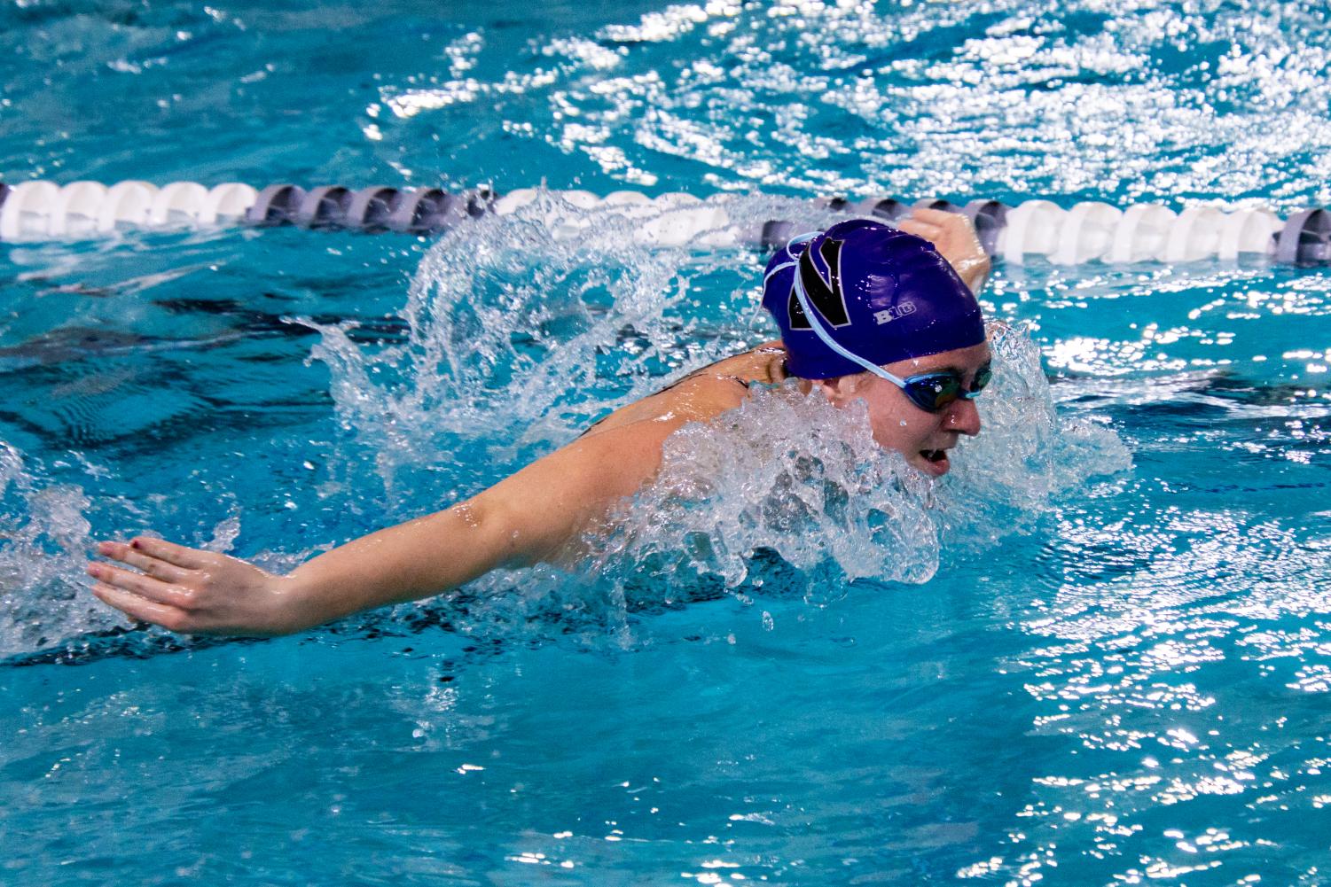 A person with a purple cap swims with their arms spread out on either side.