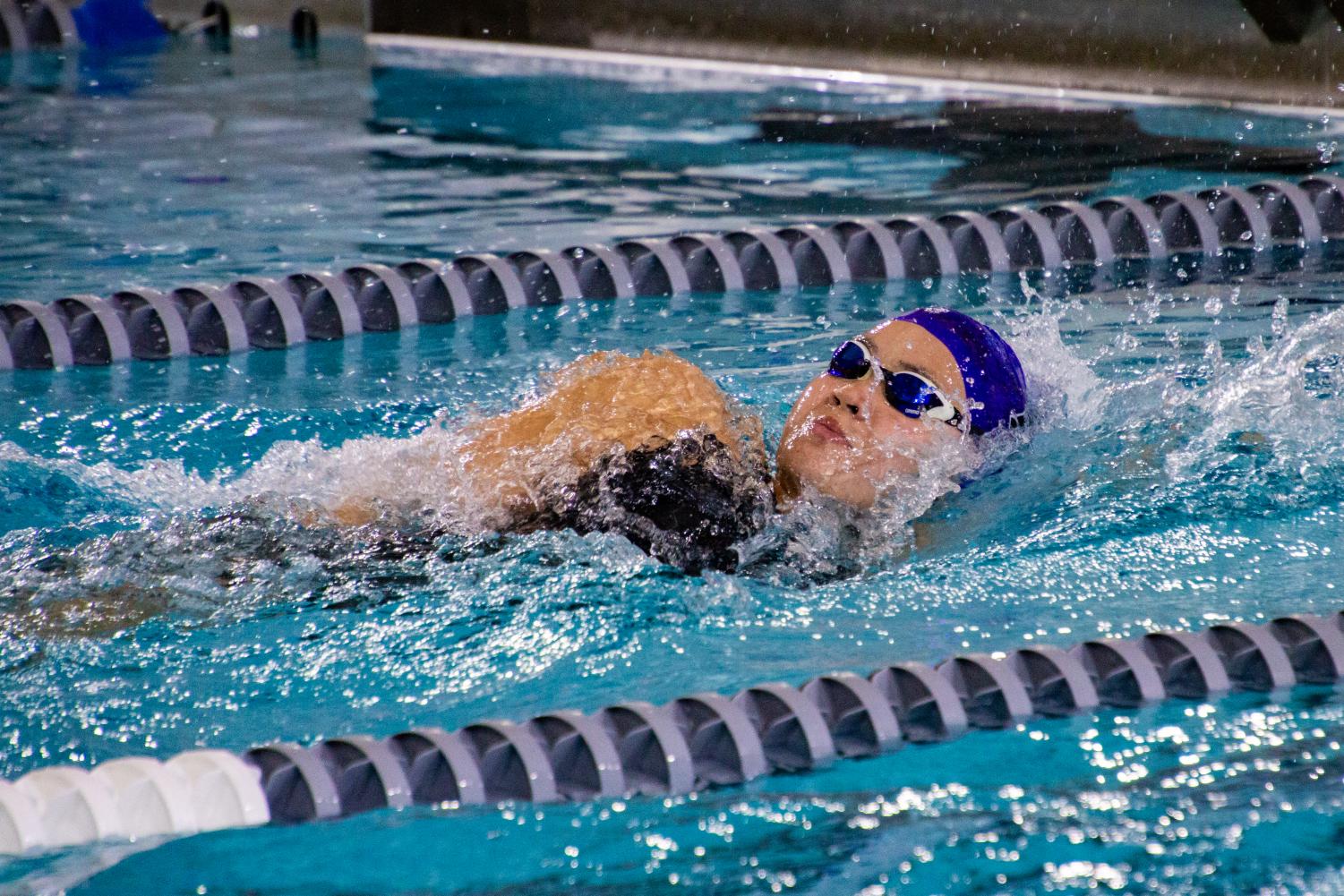 A swimmer with a purple cap comes up for a breath of fresh air.