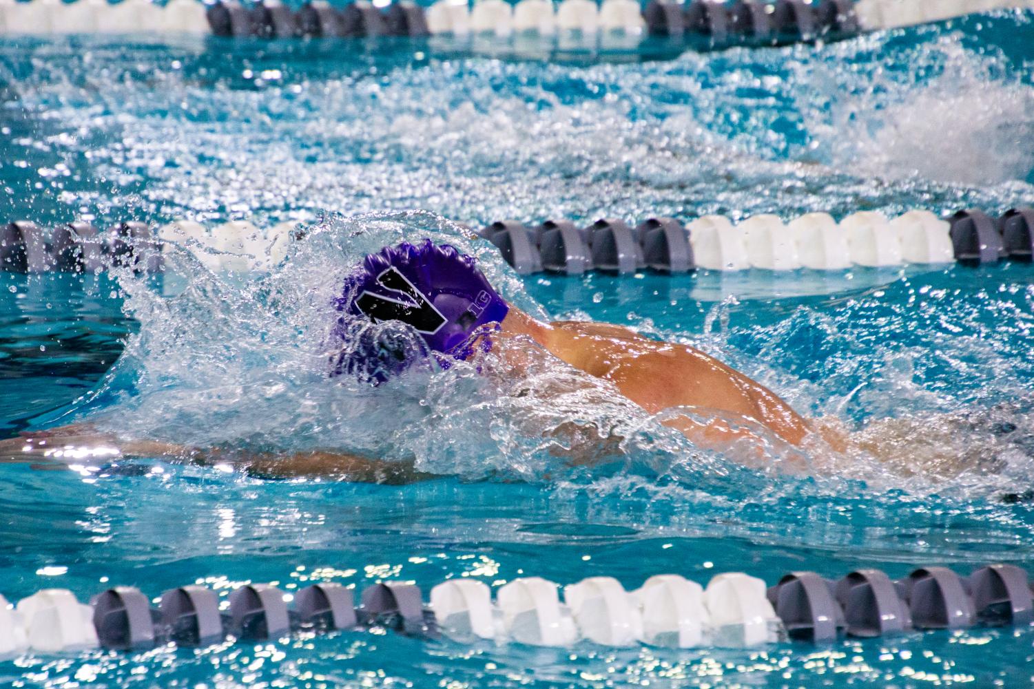 A purple cap is visible as water splashes around the swimmer.