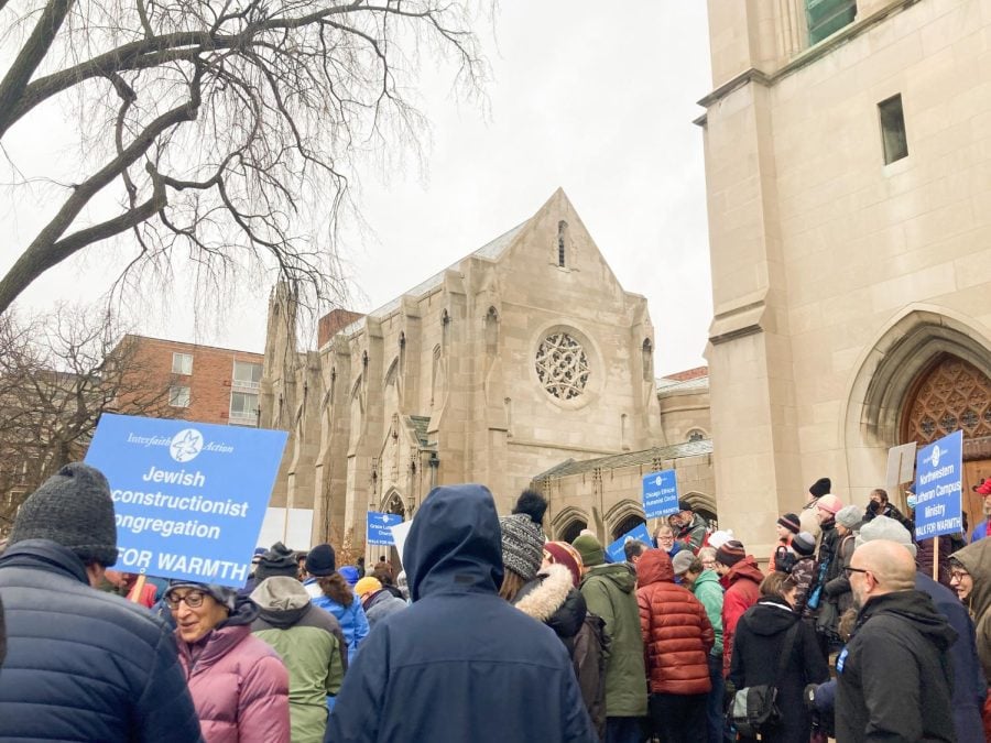 A group of people holding blue signs for religious organizations gather outside a church.