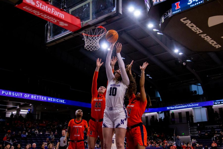 An athlete in a white jersey and white shorts shoots a layup while two athletes in orange jerseys defend her.