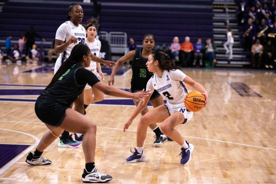 An athlete in a white jersey and white shorts dribbles a basketball with her left hand.