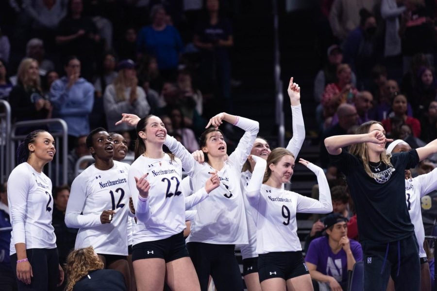 Volleyball+players+in+white+and+purple+uniforms+cheer+together+on+a+volleyball+court.