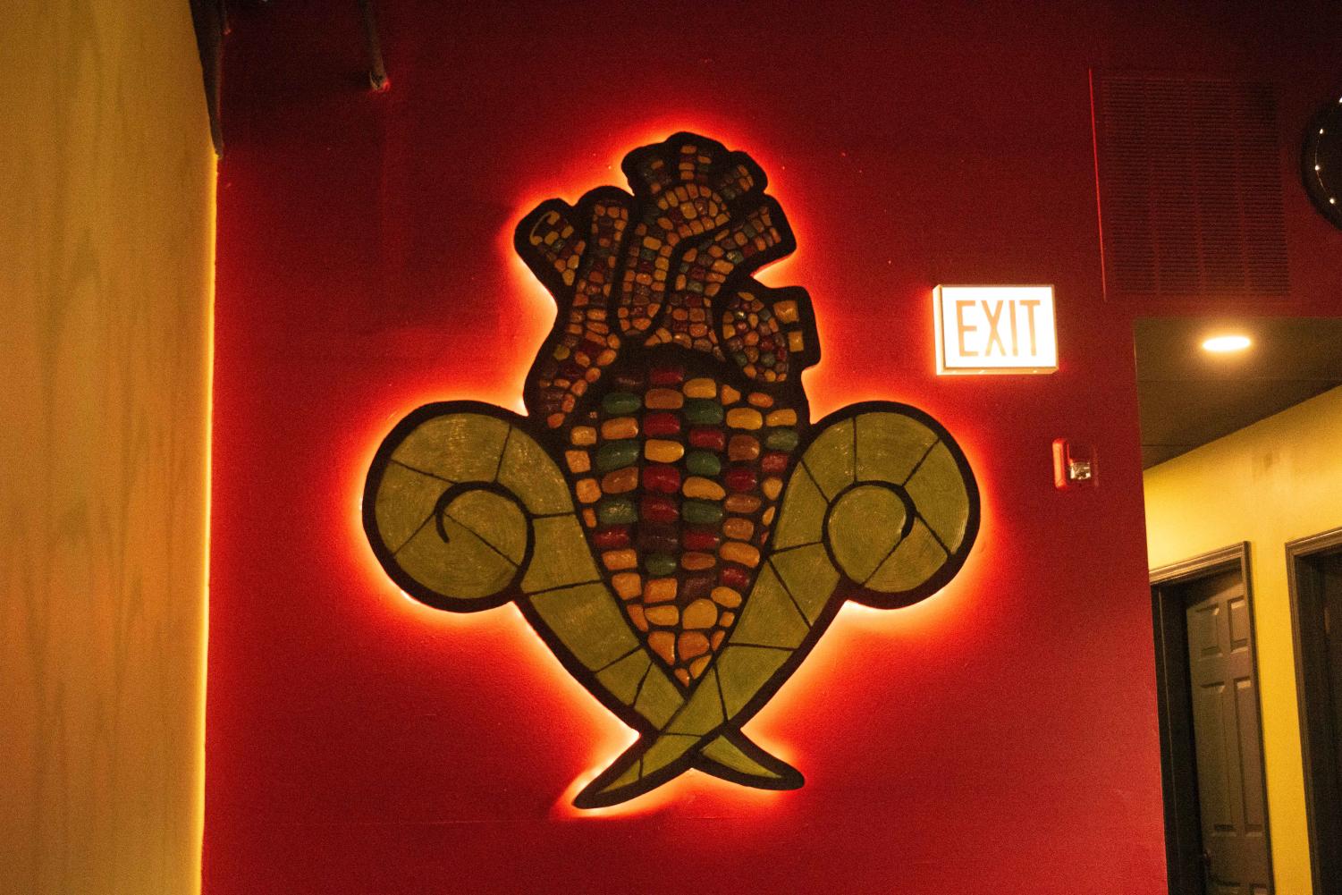 A+sculpture+of+an+ear+of+corn+shaped+like+a+heart+hangs+on+a+red+wall.