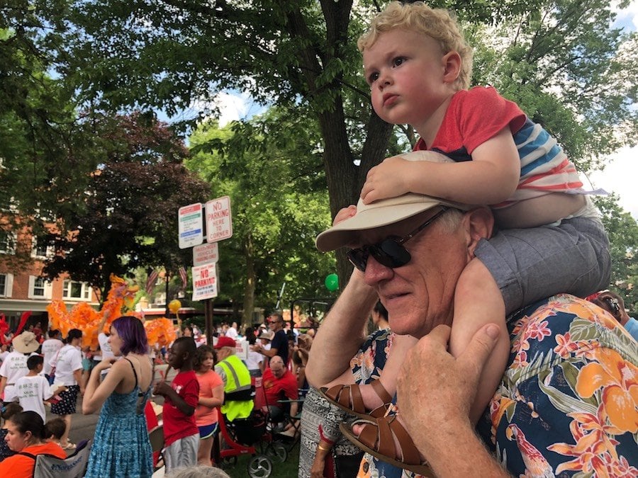 A man with a child on his shoulders watches a parade float go by.