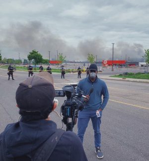 A man reporting to a camera in front of a smoky horizon.