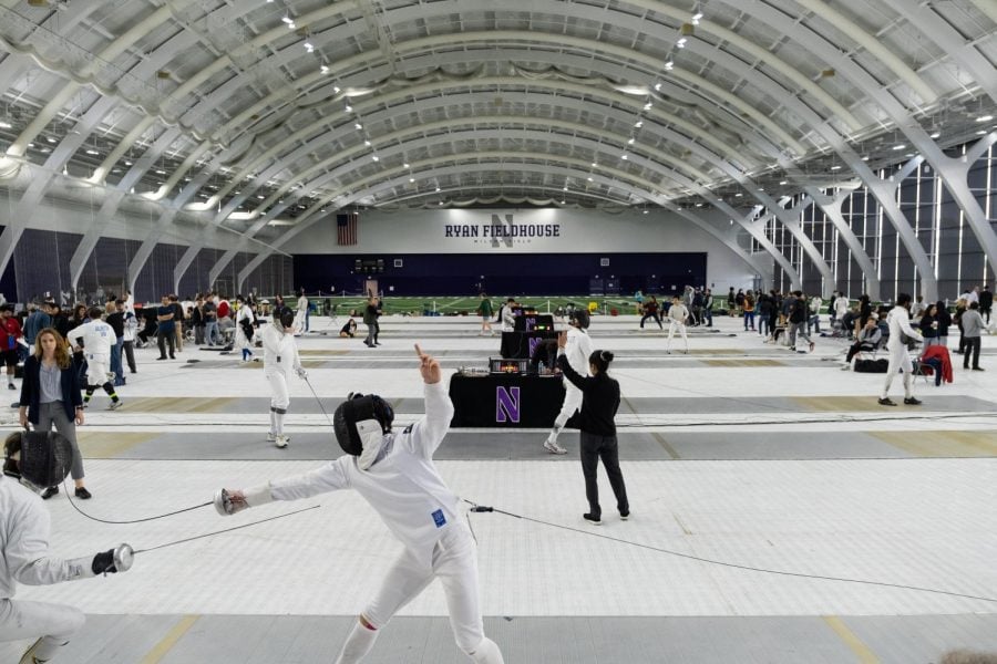 Fencing+competition+in+an+indoor+stadium+with+white+mats+lining+the+floor.