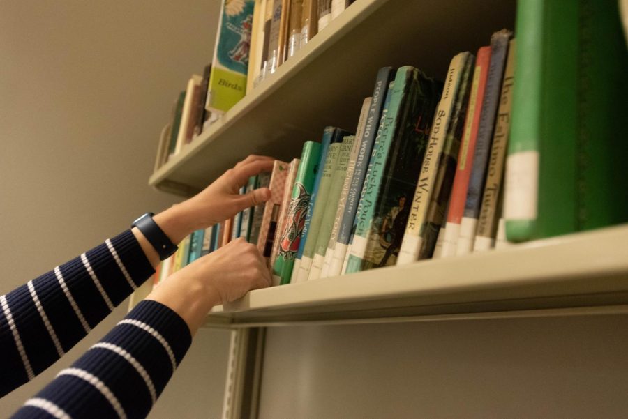 A person’s hand is grabbing a book from the shelf