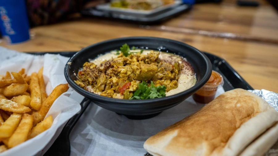 A black bowl filled with hummus and topped with chicken.