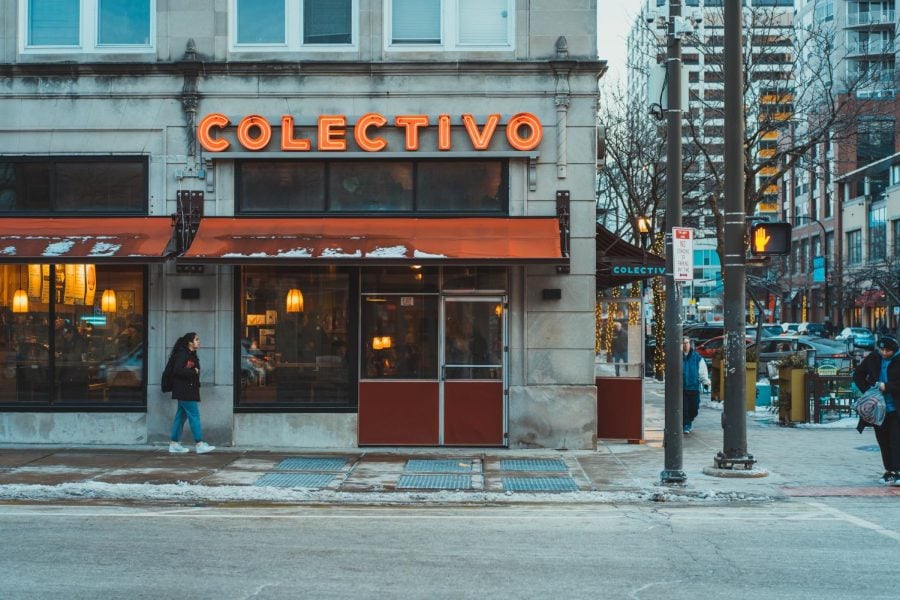 A red sign reading “Collectivo” shines over a pedestrian walking in snow.