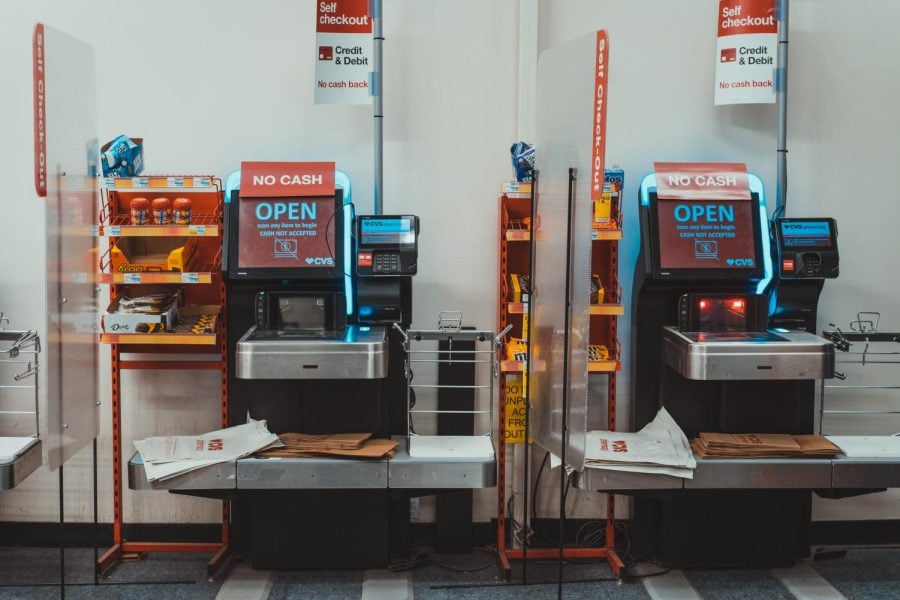 Two self-check-out machines side by side with signs on them that read “no cash.”