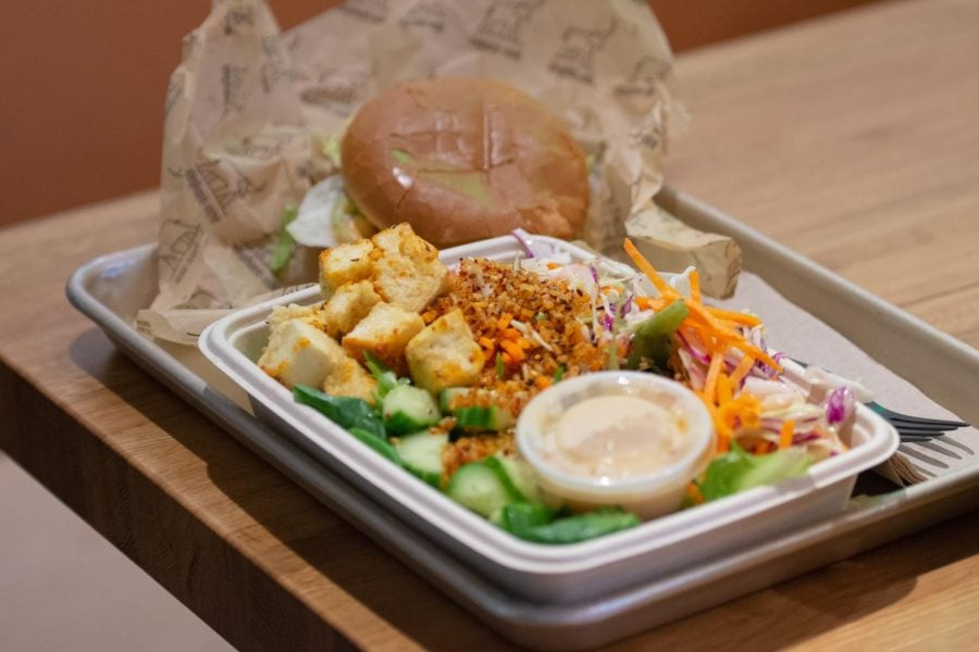 A salad with tofu and lettuce on a metal tray, and a burger in the background.