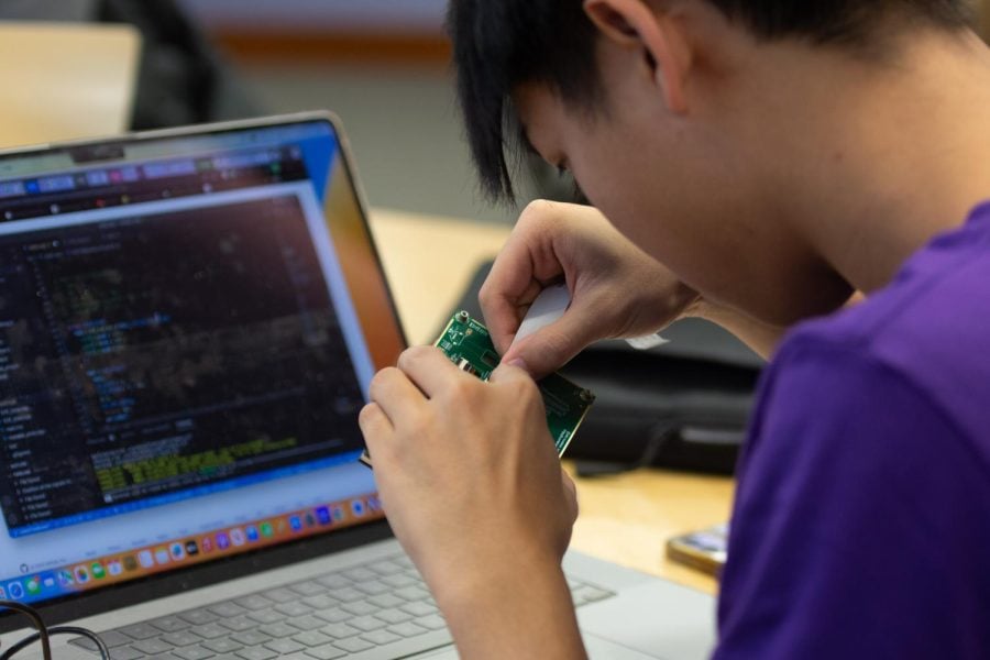 A student in a purple t-shirt works on a green circuit board.