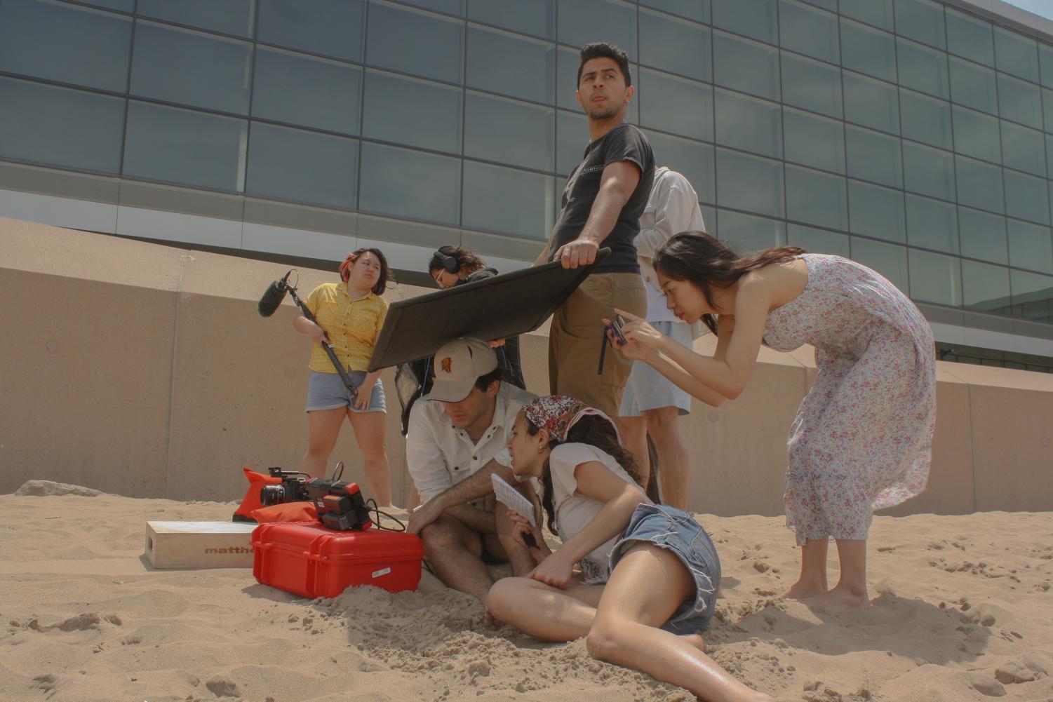 A group of people gather around a screen on a beach. 