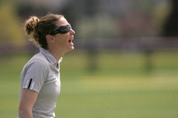 A woman in a gray shirt yells in a grass field.