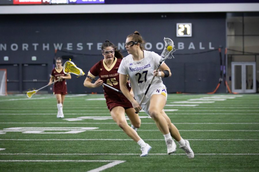 An athlete in a white jersey runs with a lacrosse stick.