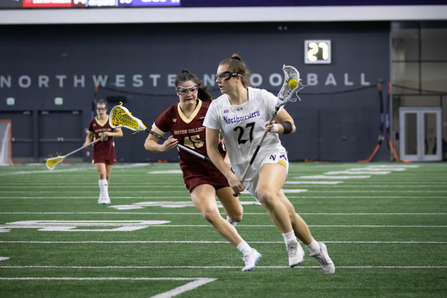 An+athlete+in+a+white+jersey+runs+with+a+lacrosse+stick.