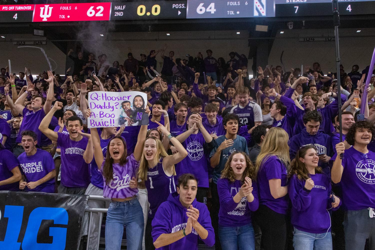 A crowd of people wearing purple cheer for a basketball game.