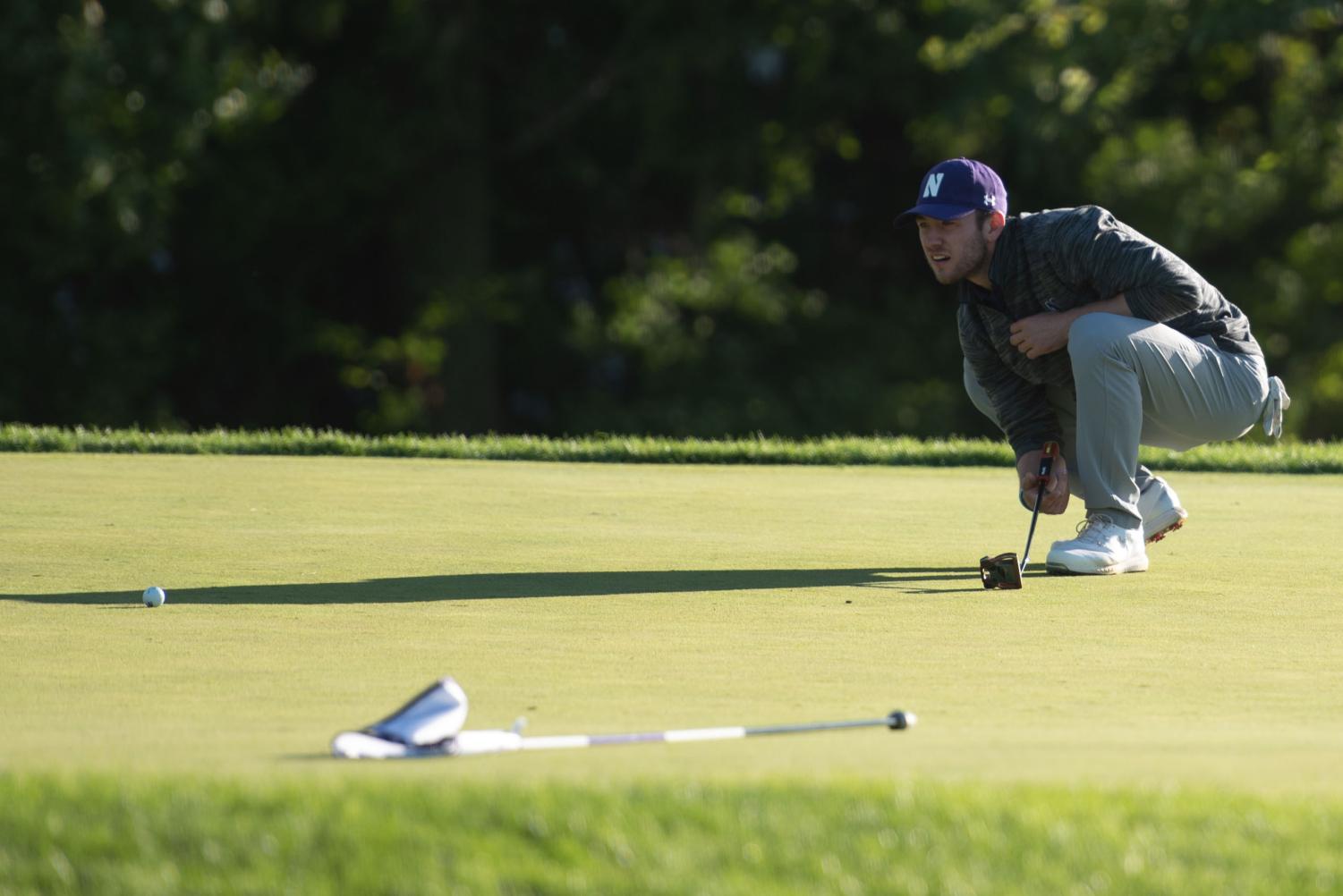 A+person+in+a+gray+shirt+and+purple+hat+looks+at+a+golf+ball+on+the+ground.