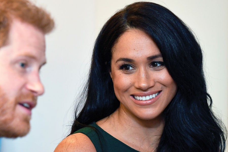 Meghan Markle smiling, looking at her husband, Prince Harry, who is seated to her right.