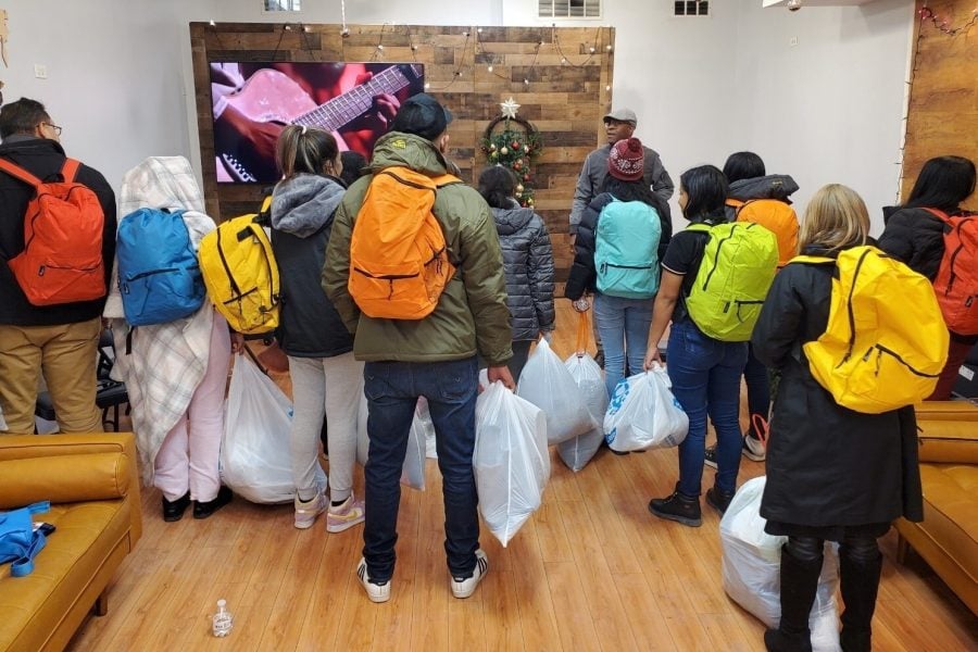 Several people stand with colorful backpacks and garbage bags, with their backs to the camera.