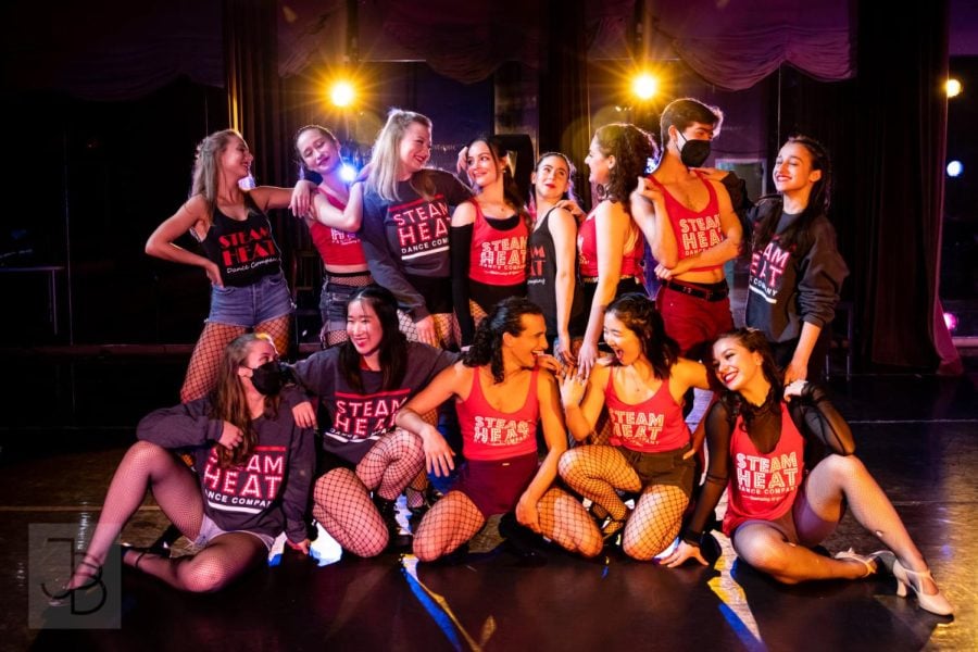 Dancers in red or gray tops and fishnet stockings pose as a group.