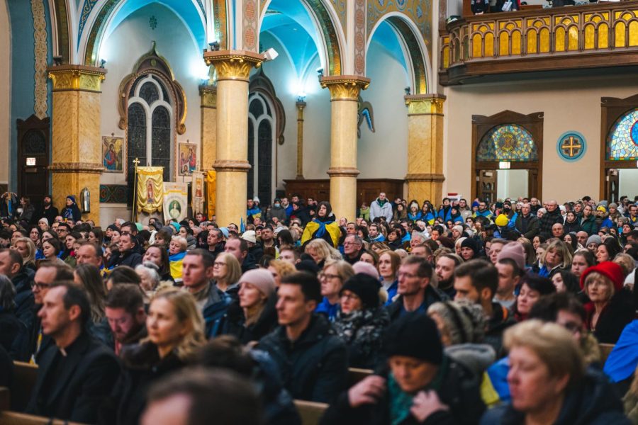 A crowd of people sits in a church with some people wearing blue and yellow flags.