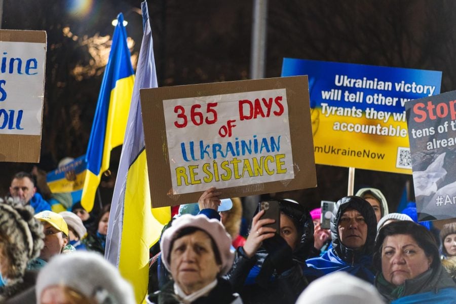 Protesters are holding posters. The central sign says: “365 days of Ukrainian Resistance,” written with blue and yellow colors of the Ukrainian flag.