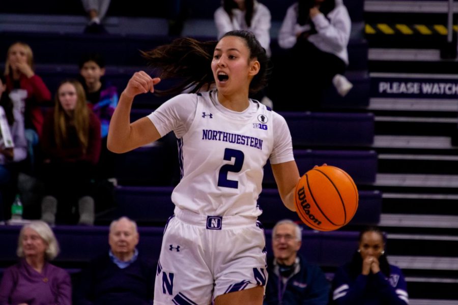 An athlete in a white jersey dribbles a basketball with her left hand.