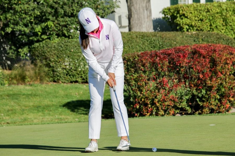A golfer in white clothes hits a golf ball with a golf putter.