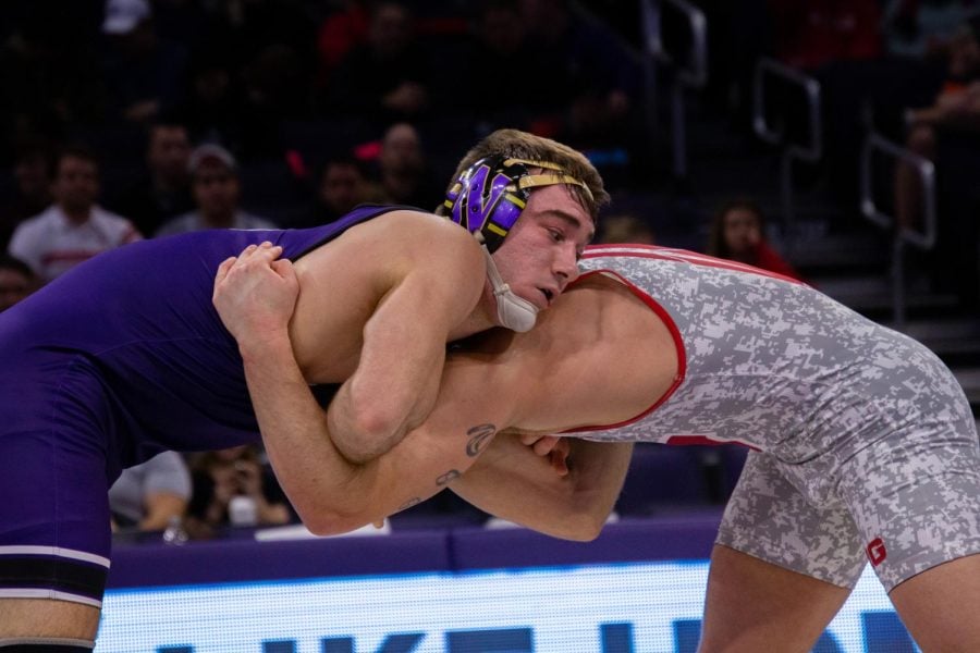 A wrestler in a purple singlet wrestles his opponent in a gray camouflage singlet.