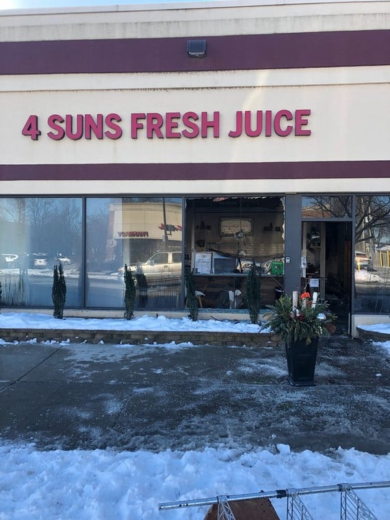 Lettering above a store says “4 Suns Fresh Juice.” One of the store’s windows is broken.