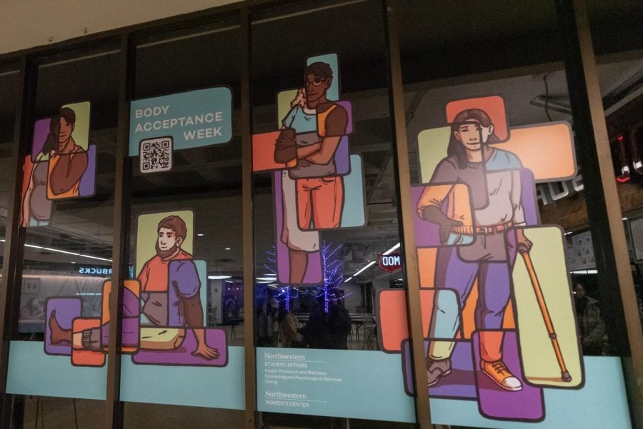 A window with multi-colored graphics of people and the words “Body Acceptance Week.”