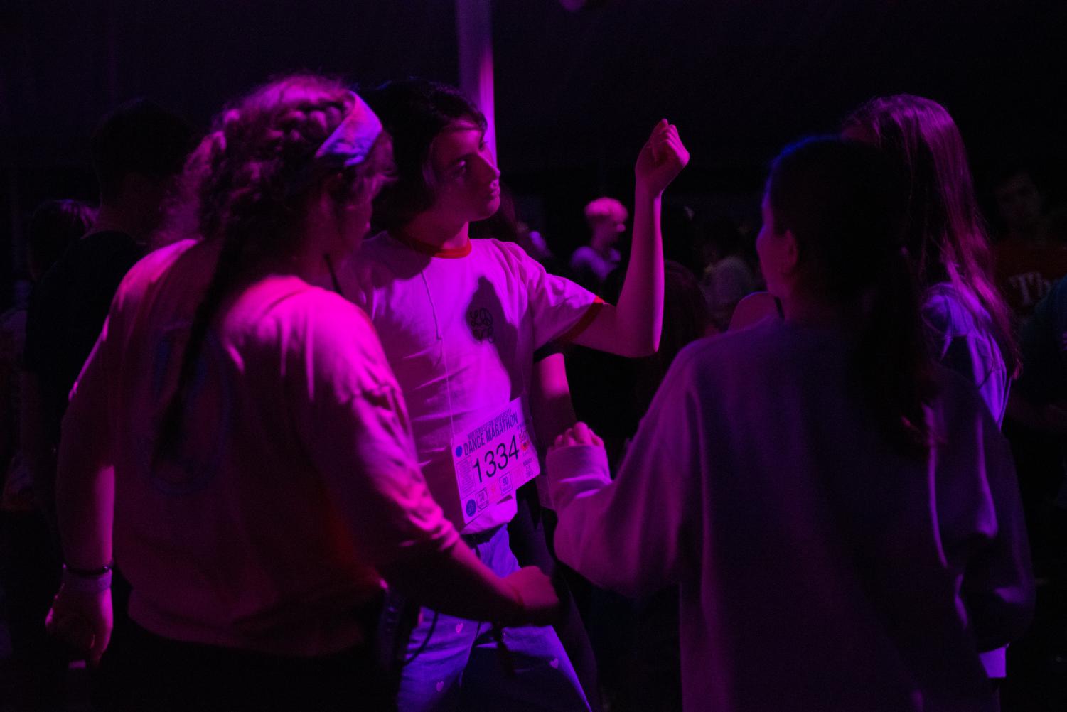 Multiple people dance in a dimly lit room. 
