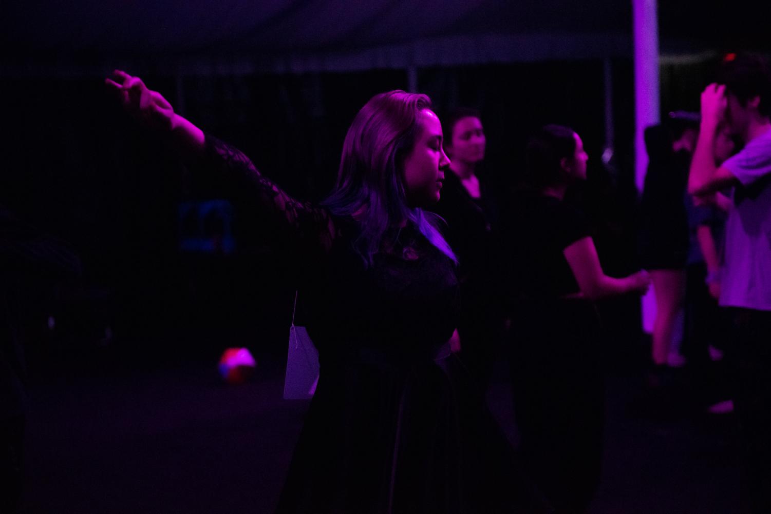 A person dances under purple lights, their arm outstretched. 