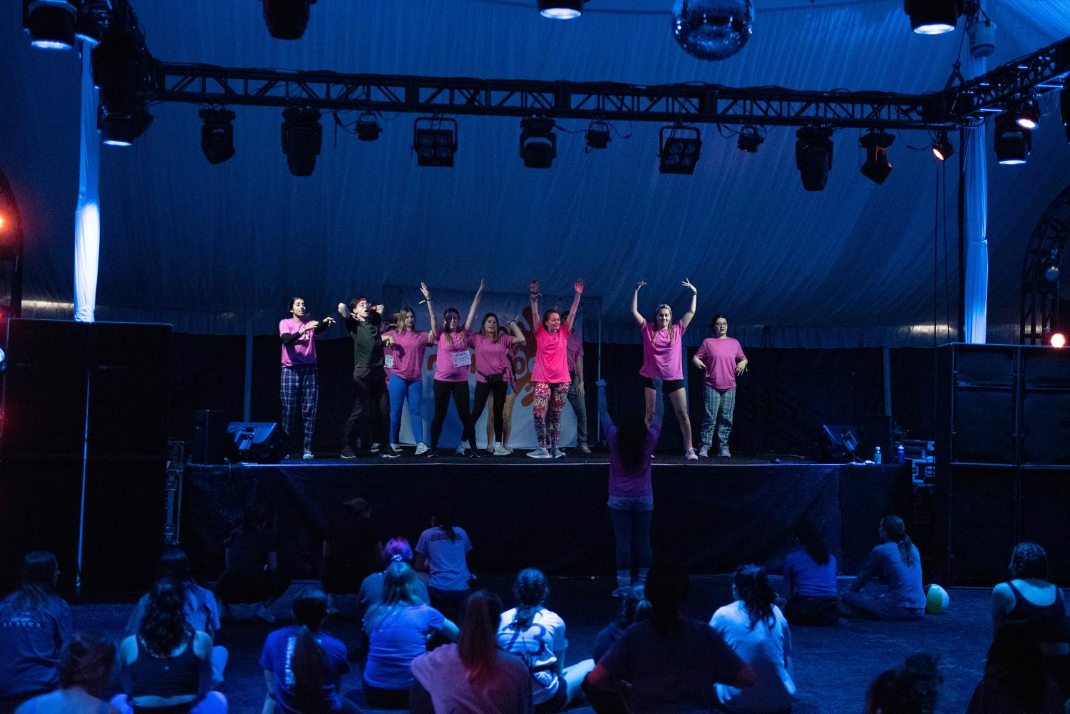People in pink stand on the stage with their arms in the air.
