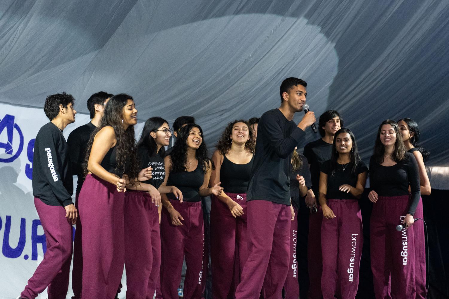 A group of people dance onstage wearing black shirts and maroon pants.