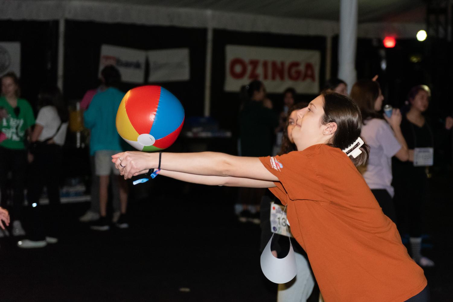 A person in an orange shirt extends two arms to hit a colorful beach ball. 