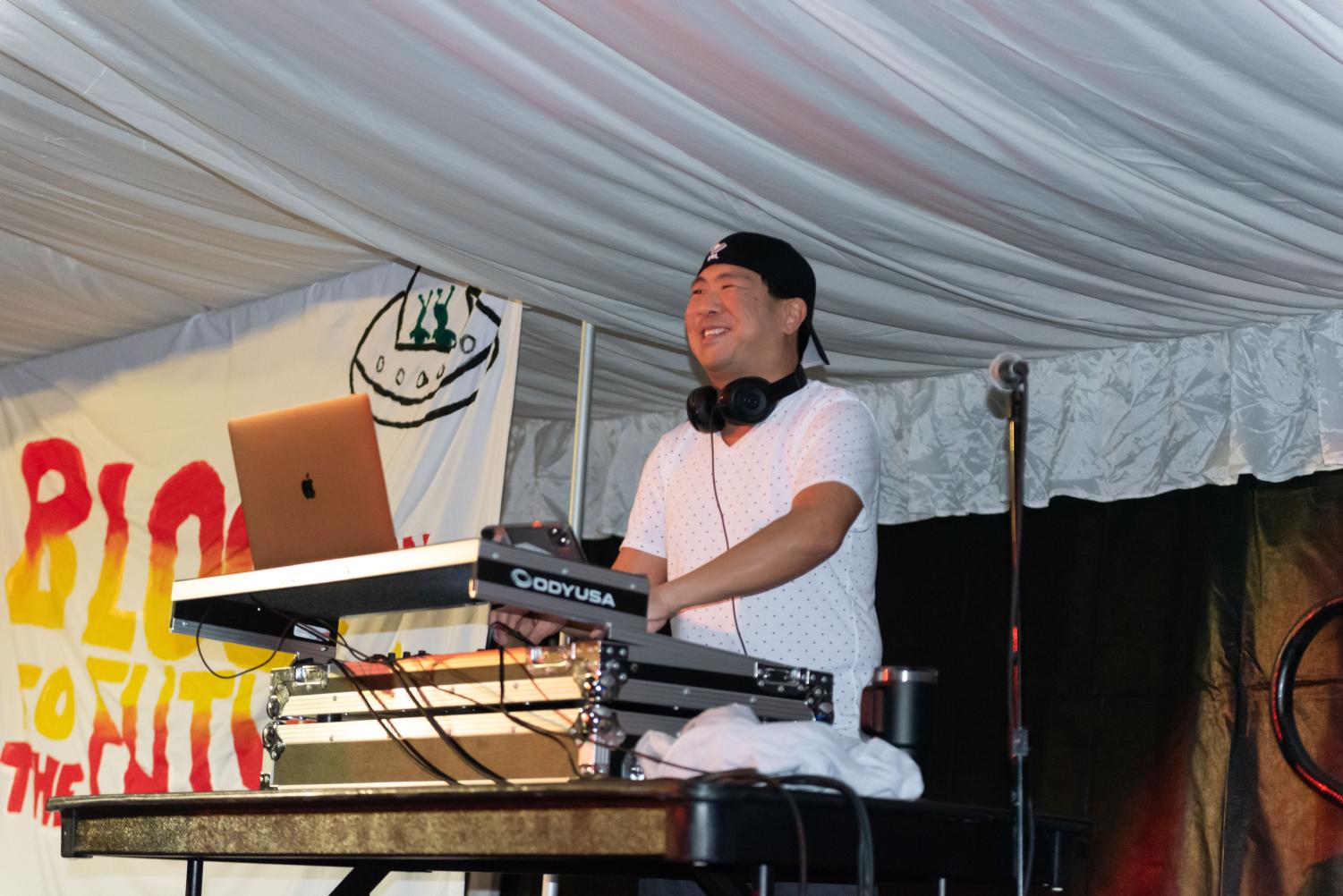 A DJ behind a laptop stands in front of a banner saying “Block to the Future.”